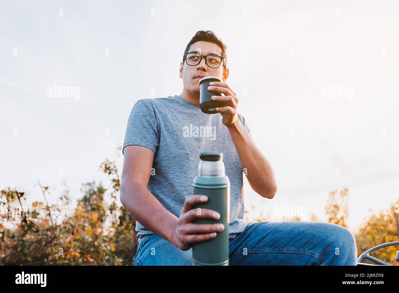 Uomo contadino latino che beve compagno e rilassarsi, in uno spazio rurale, sulla cima di un vecchio trattore piccolo. Bevanda calda Foto Stock