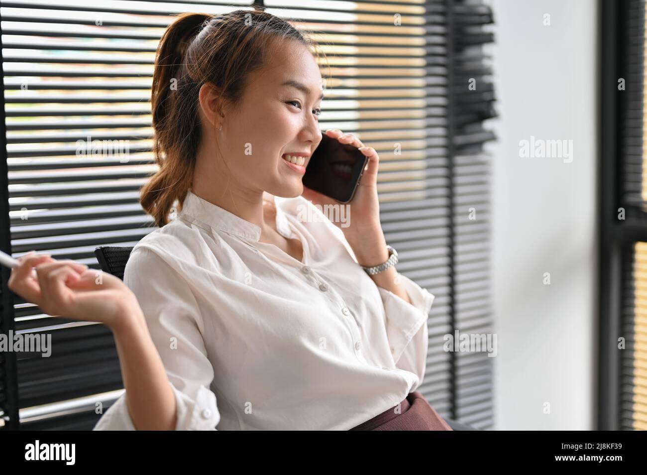 Una donna d'affari asiatica allegra o una lavoratrice femminile godono di parlare al telefono con il suo amico durante la pausa pranzo in ufficio. Foto Stock