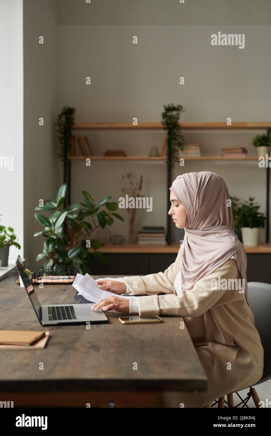 Immagine verticale laterale della giovane donna musulmana che lavora come contabile che fa lavoro di documentazione Foto Stock