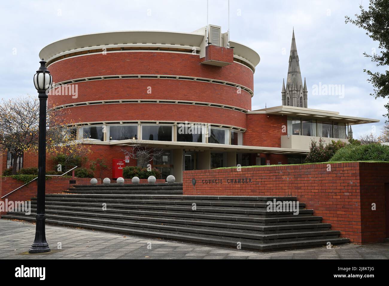 Circular Brighton Municipal Offices Building, sede della Bayside Council Chamber, vista dal livello della strada, con campanile della chiesa sullo sfondo Foto Stock