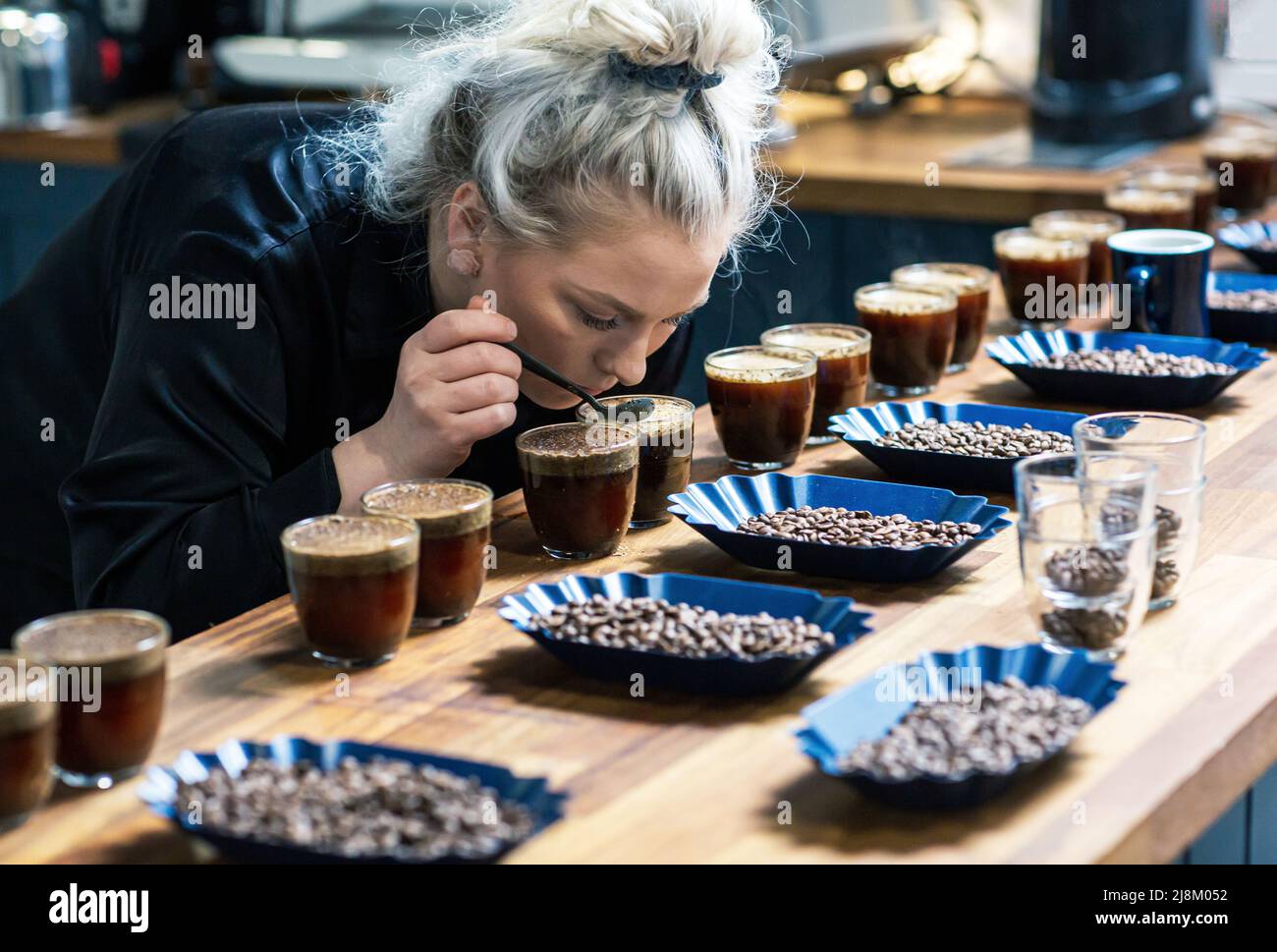Il processo di cupping. Donna degustazione di caffè appena fatto con cucchiai. Accessori per il caffè sul tavolo. Foto Stock