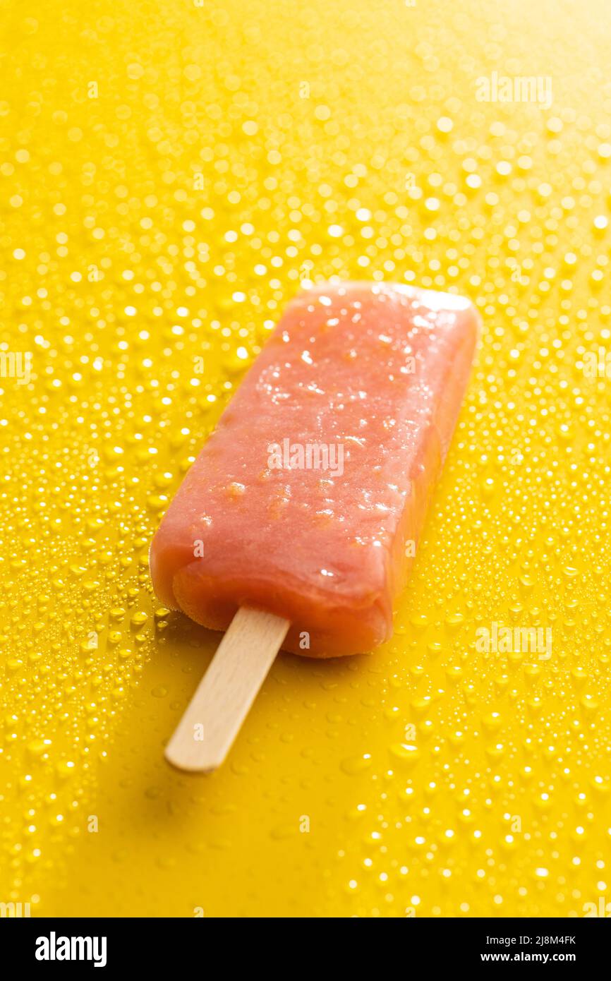 Ghiacciato fruttato. Dolce pop cicle su tavola gialla con gocce d'acqua. Foto Stock
