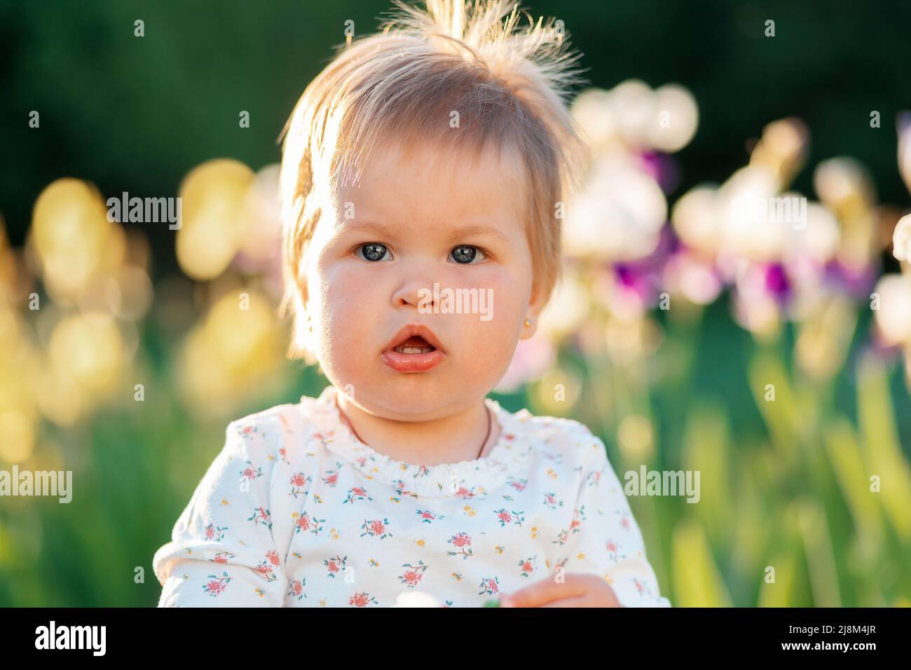 Ritratto di una ragazza caucasica carina grattacata. Iridi bloomining sfocati sullo sfondo. Concetto di giornata dei bambini felici. Foto Stock