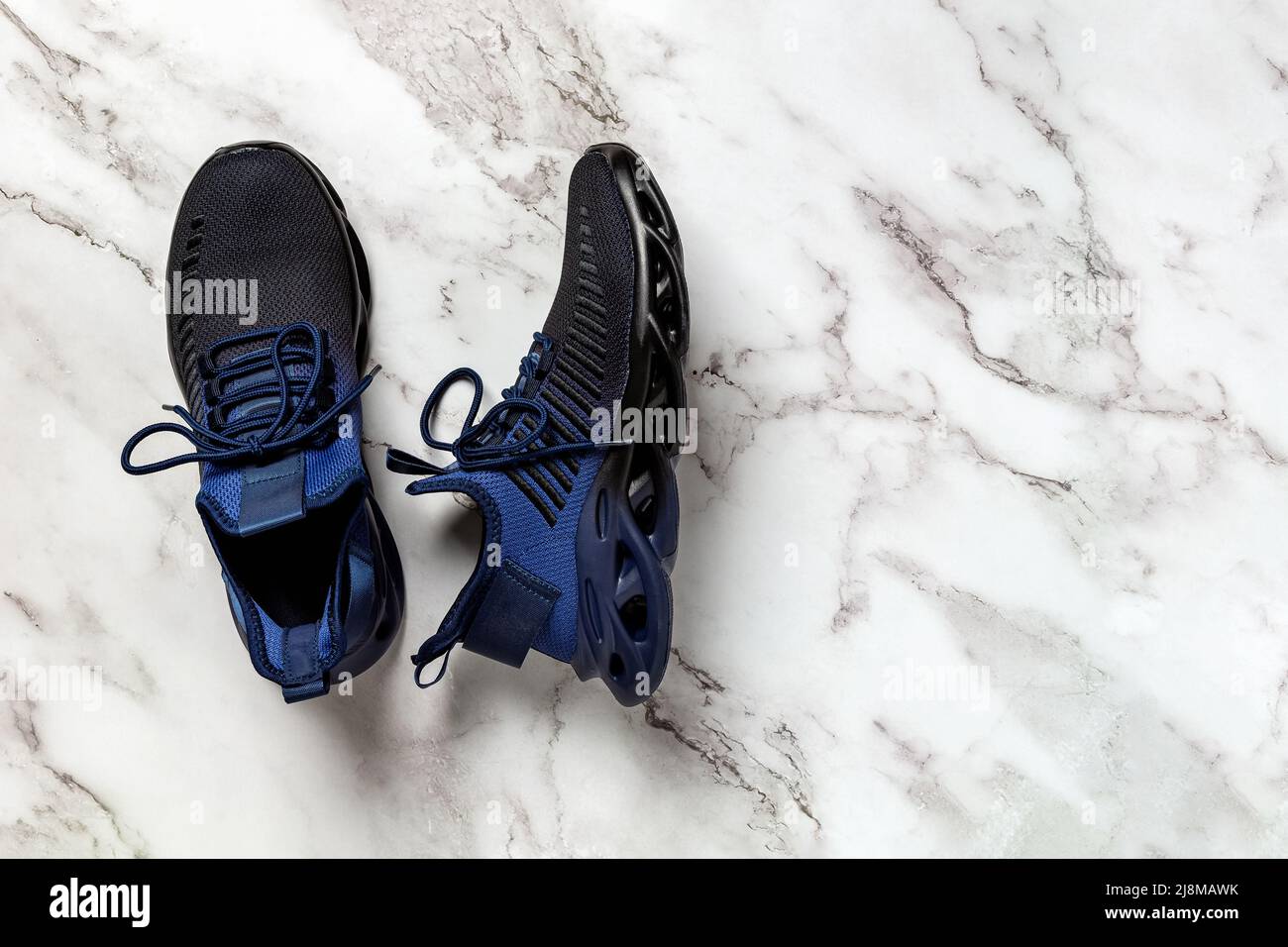 Scarpe da uomo con lacci e scanalature su un pavimento in marmo. Un paio di  sneaker in tessuto mesh blu nero per il fitness e lo stile di vita attivo.  Nuove sneakers
