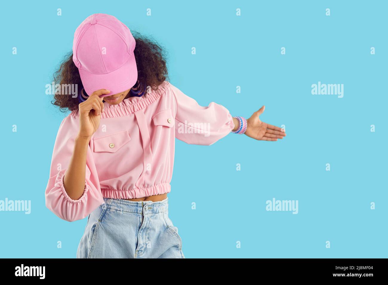 Il bambino nero in berretto di baseball rosa alla moda mostra qualcosa sullo sfondo blu dello spazio delle copie Foto Stock