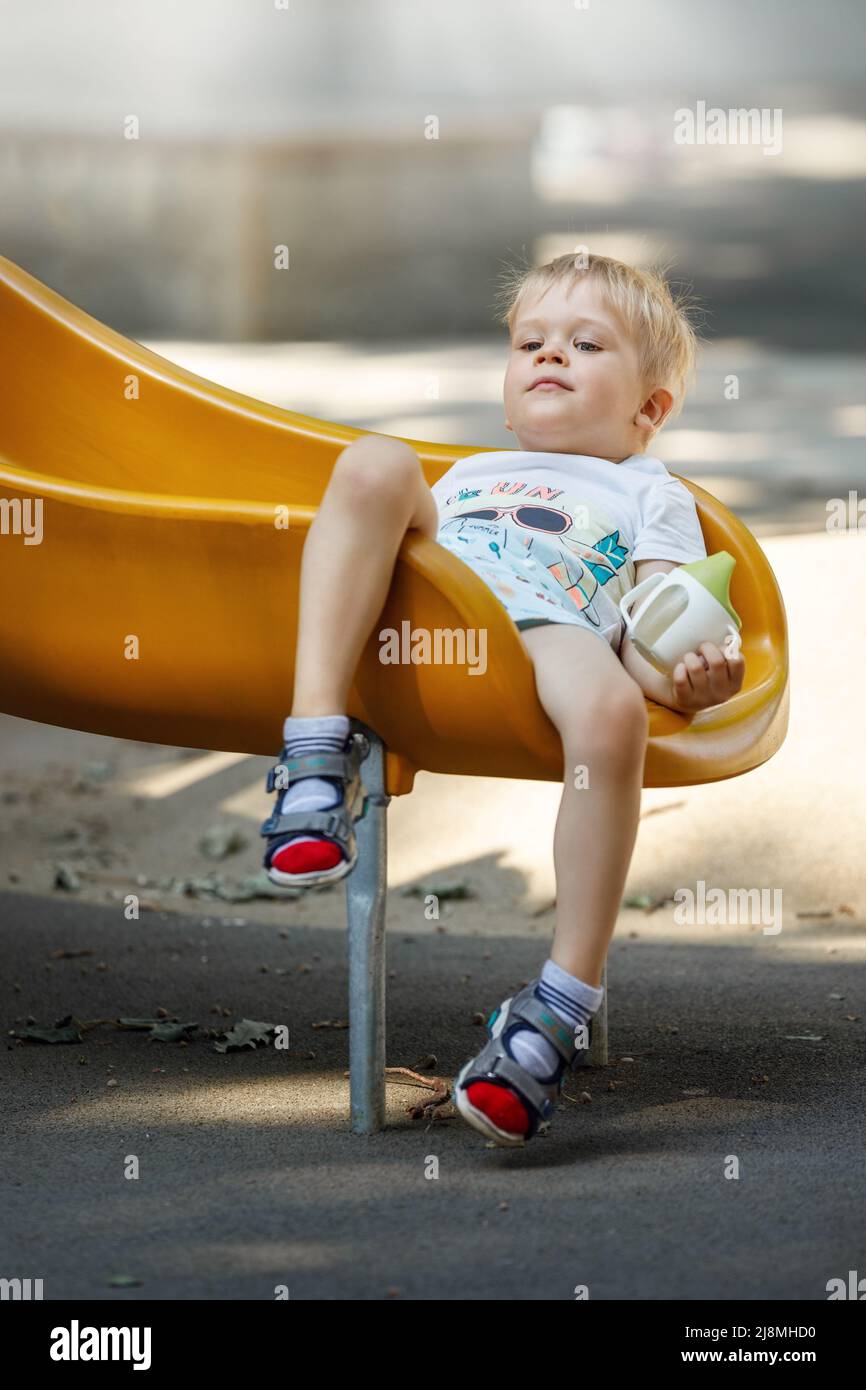 Il ragazzo scivola in un cursore di plastica giallo, i suoi capelli diventano eclettici, il bambino si trova comodamente per riposare. Foto Stock