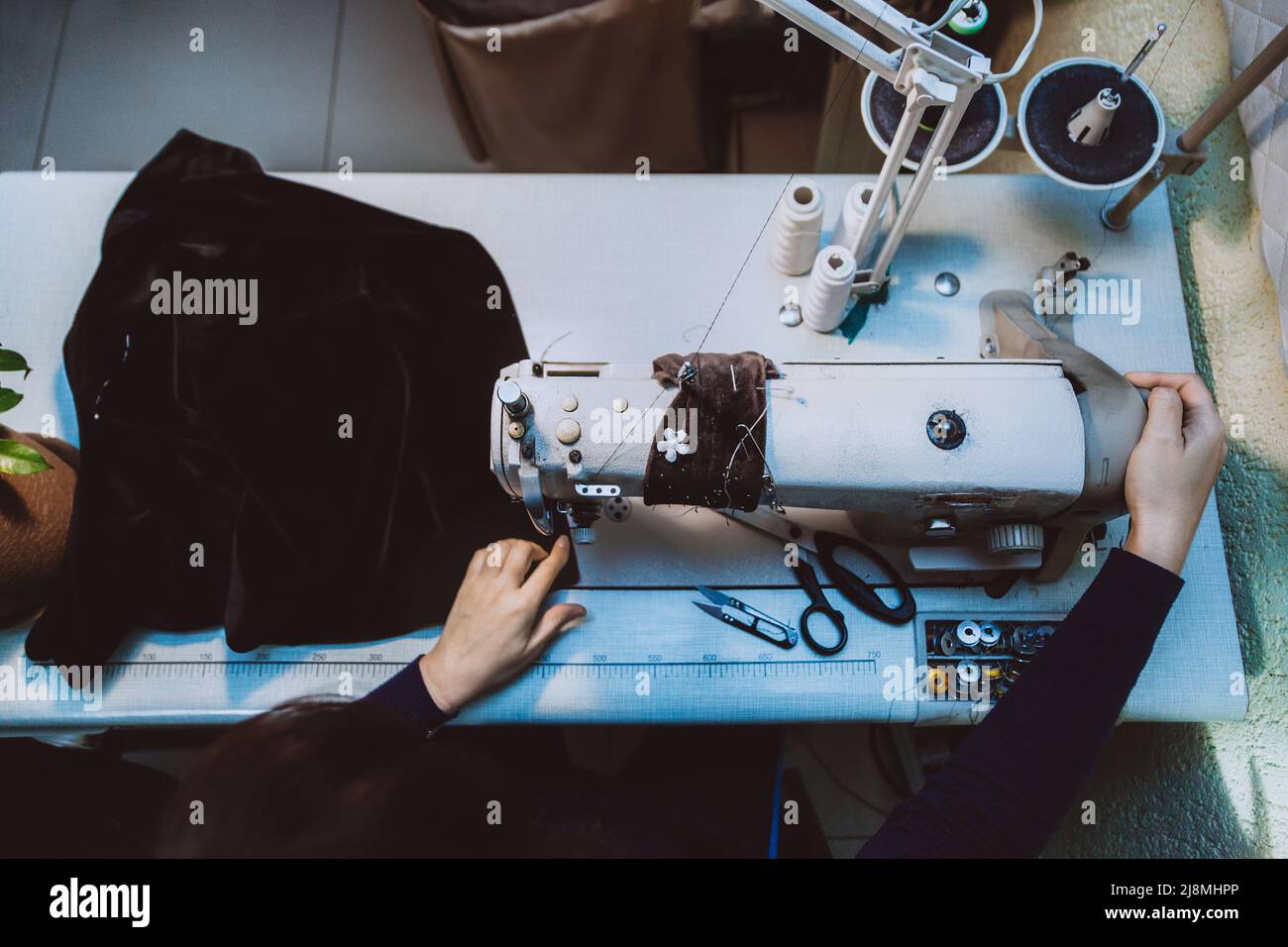 Una donna cucita abiti su misura - una giacca alla moda in tessuto di velluto su una macchina da cucire nel suo atelier, vista dall'alto Foto Stock