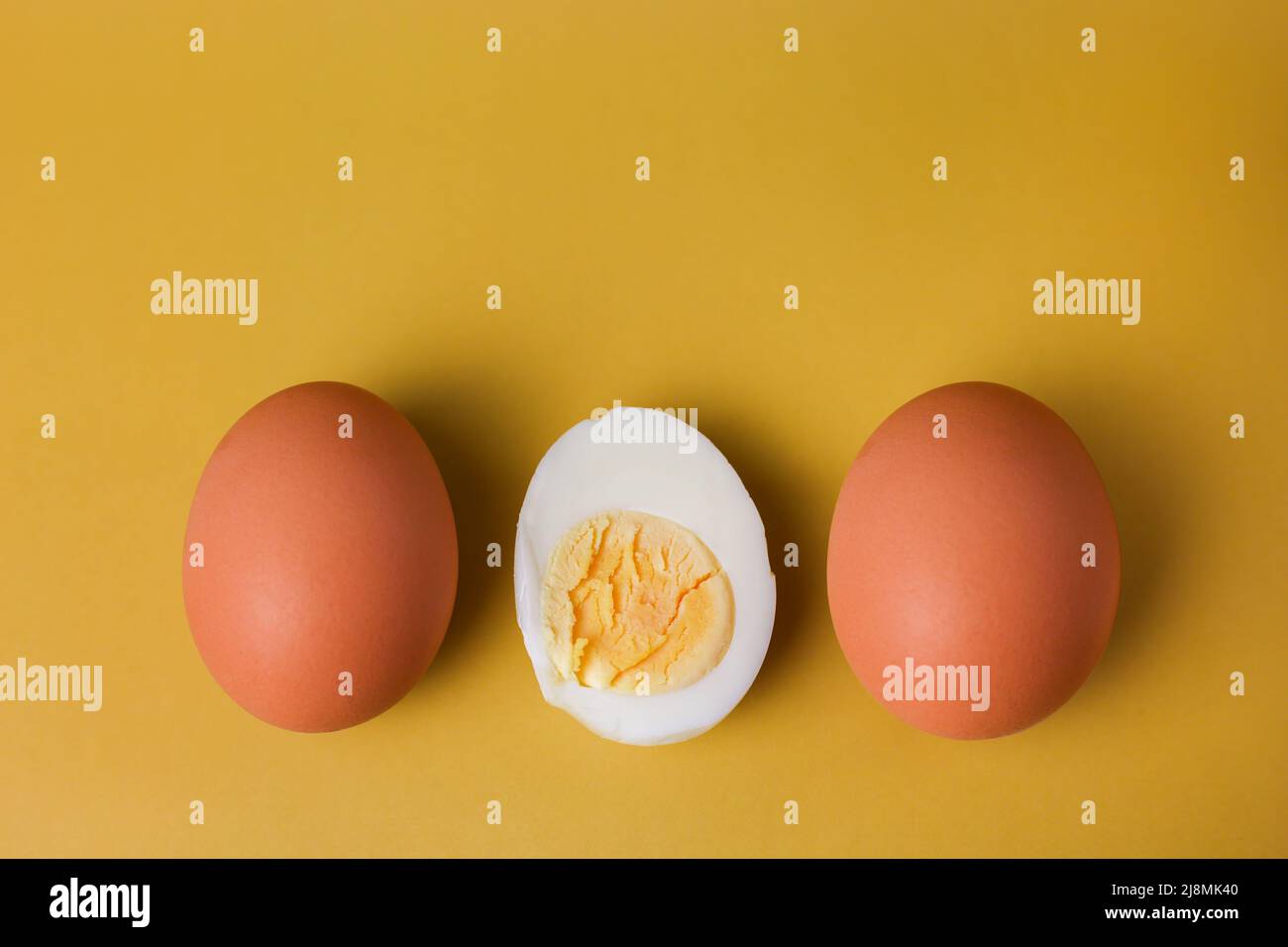 Due uova intere marroni e un uovo sode con tuorlo tagliato a metà su un fondo isolato di giallo chiaro Foto Stock