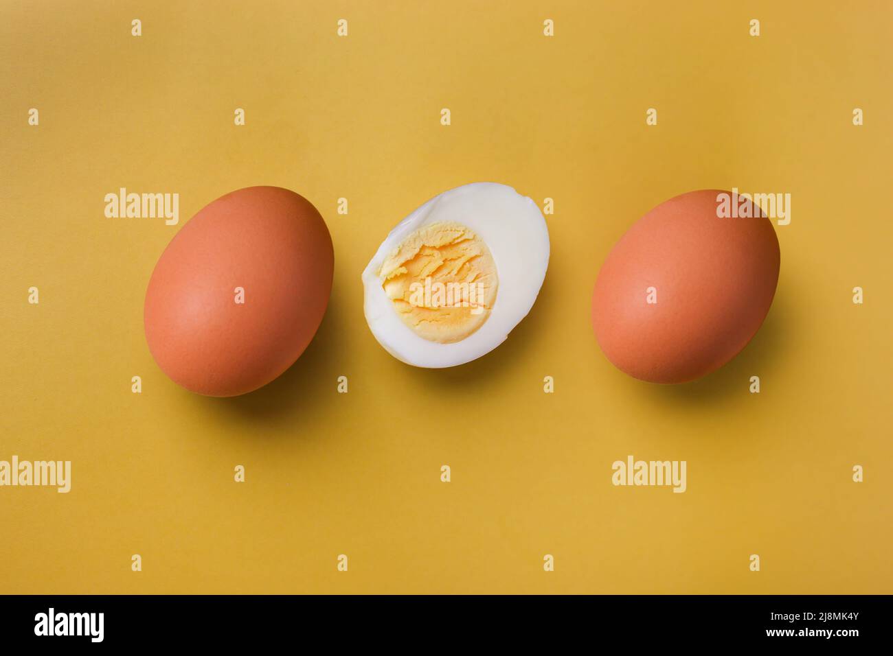 Due uova intere marroni e un uovo sode con tuorlo tagliato a metà su un fondo isolato di giallo chiaro Foto Stock
