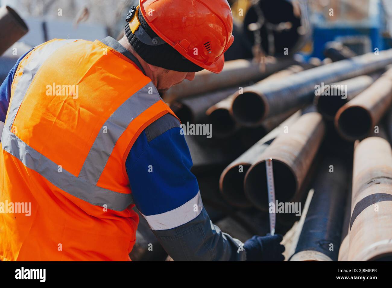 Costruttore in casco e gilet misura il diametro del tubo. Flusso di lavoro. Magazzino aperto con tubi metallici. Foto Stock