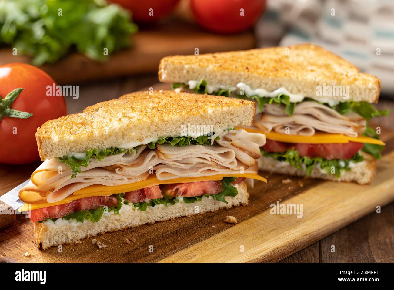 Panino a fette con tacchino, formaggio, lattuga e pomodoro su pane tostato tagliato a metà su un tagliere Foto Stock