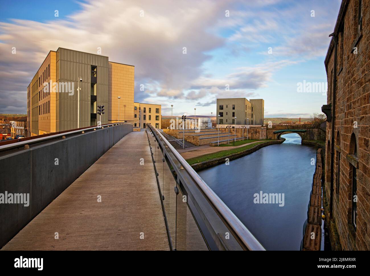 Guardando lungo un ponte pedonale che attraversa il canale di Leeds e Liverpool, verso Sandygate Halls, Burnley College, UCLAN Foto Stock