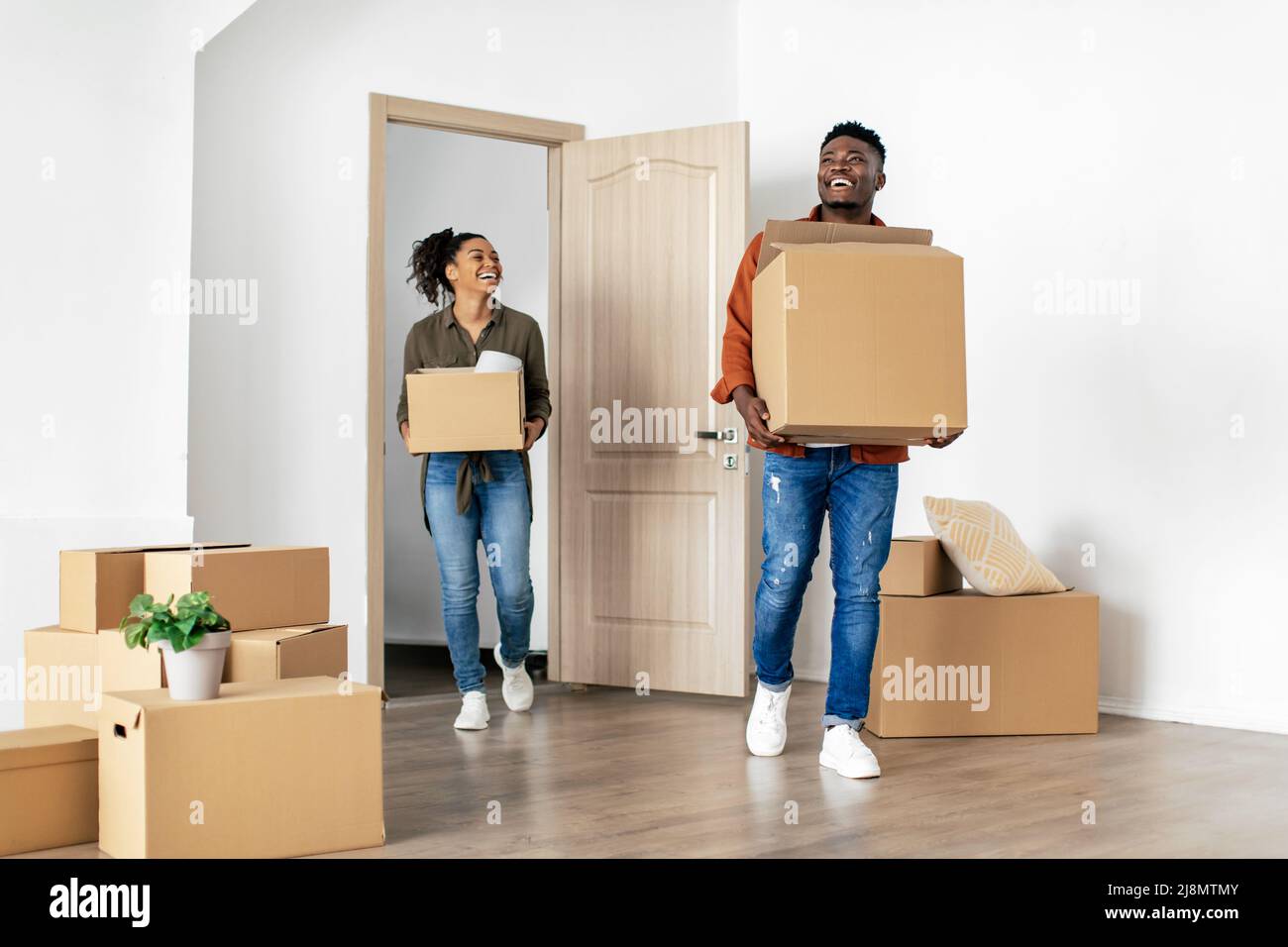Gioiosa coppia afroamericana che entra in casa portando scatole in movimento Foto Stock