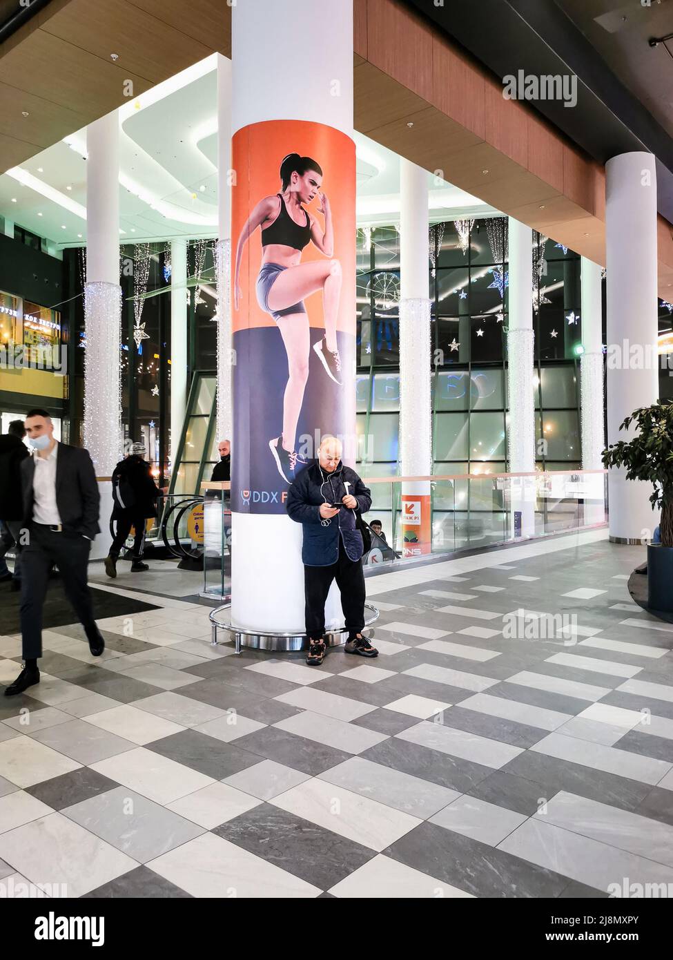 Mosca. Russia. Febbraio 3, 2022. Un uomo in un centro commerciale utilizza uno smartphone di fronte a una pubblicità per attrezzature sportive. Foto Stock
