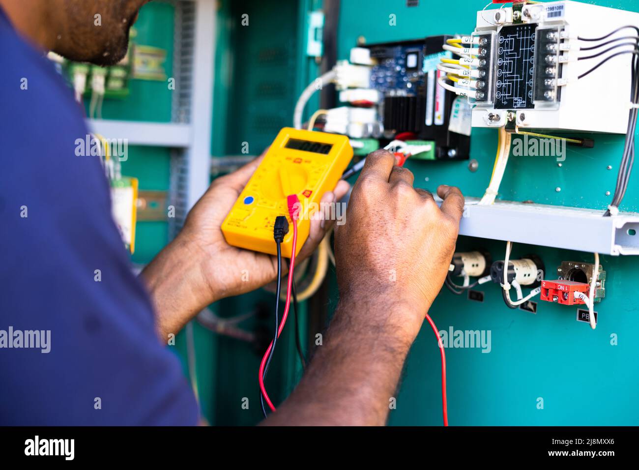 Tecnico elettrico a spalla o riparatore che controlla il collegamento utilizzando il voltmetro sul quadro di distribuzione dell'alimentazione dell'azienda industriale - concetto di Foto Stock