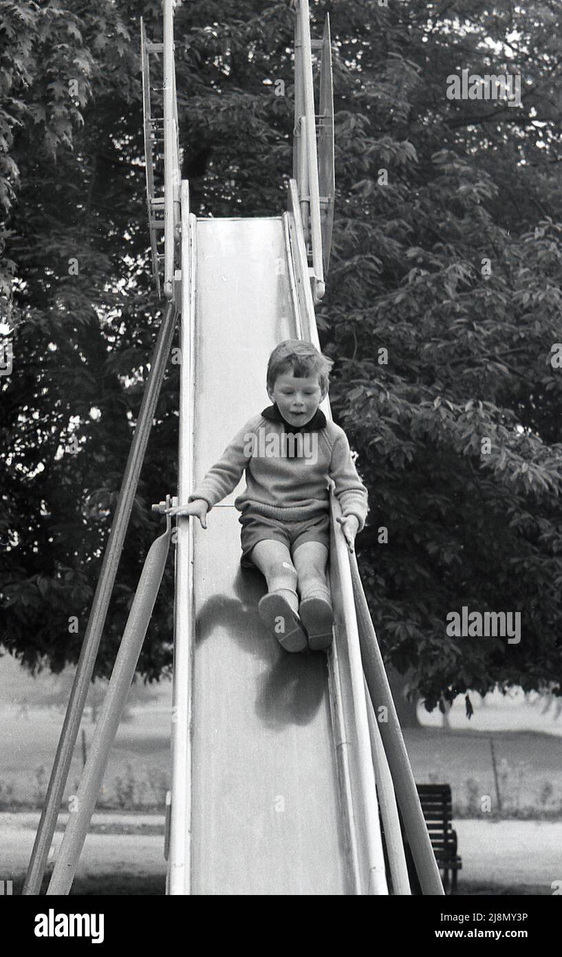 1970s, storico, un giovane ragazzo che scende lungo uno scivolo di metallo, piedi prima sul suo fondo, Inghilterra, Regno Unito. Foto Stock