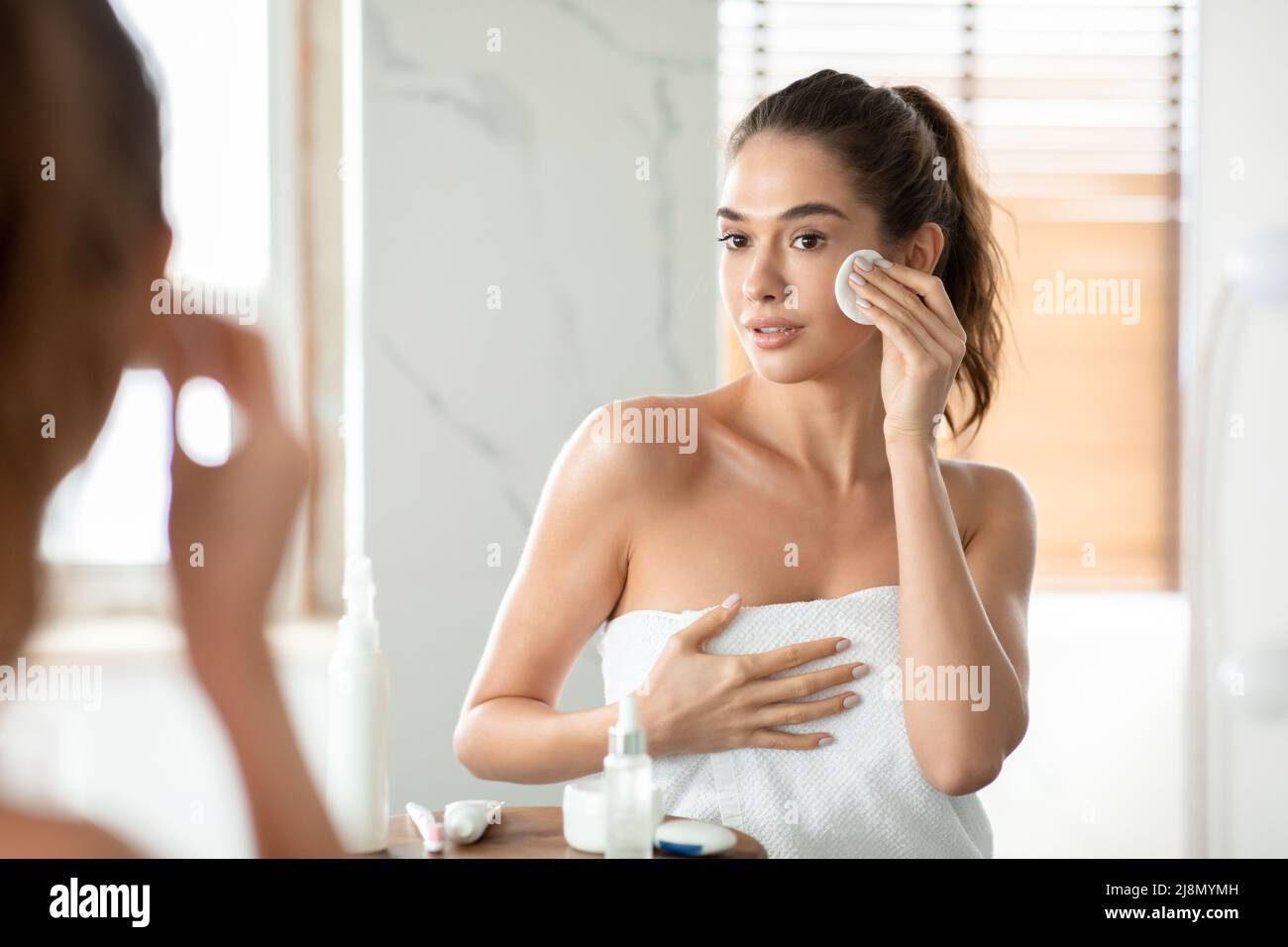 Graziosa donna che usa il tampone di cotone che pulisce la pelle facciale in bagno Foto Stock