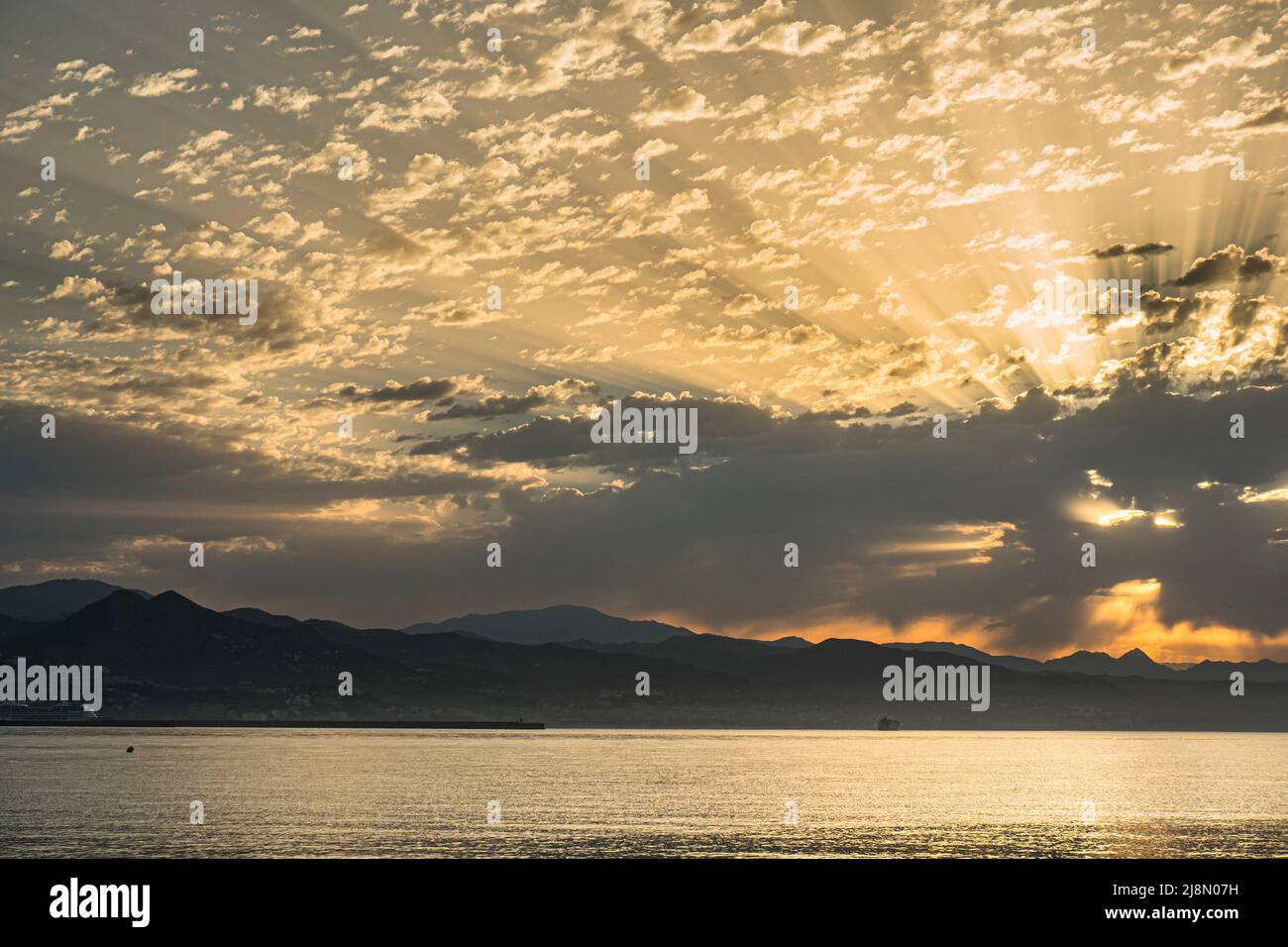 Alba estiva, con skyline di montagna e luce del sole dorata che si infrangono attraverso le nuvole tempestose. Costa del Sol, Malaga, Spagna. Foto Stock