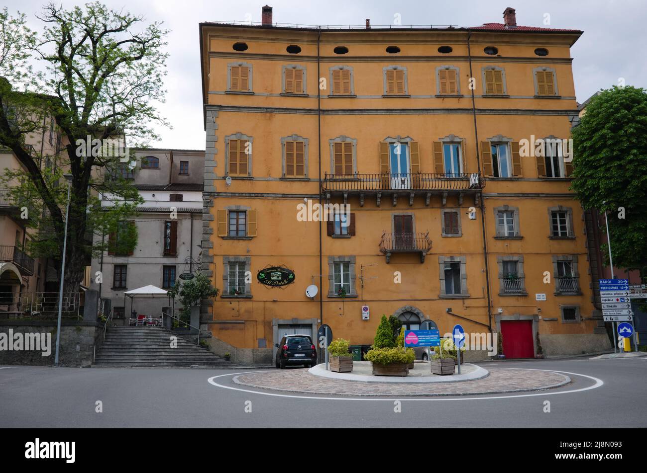Borgo Val di Taro, Italia - Maggio, 2022: Antico edificio giallo a più piani in tipico stile italiano con persiane in legno sulle finestre alla rotonda Foto Stock
