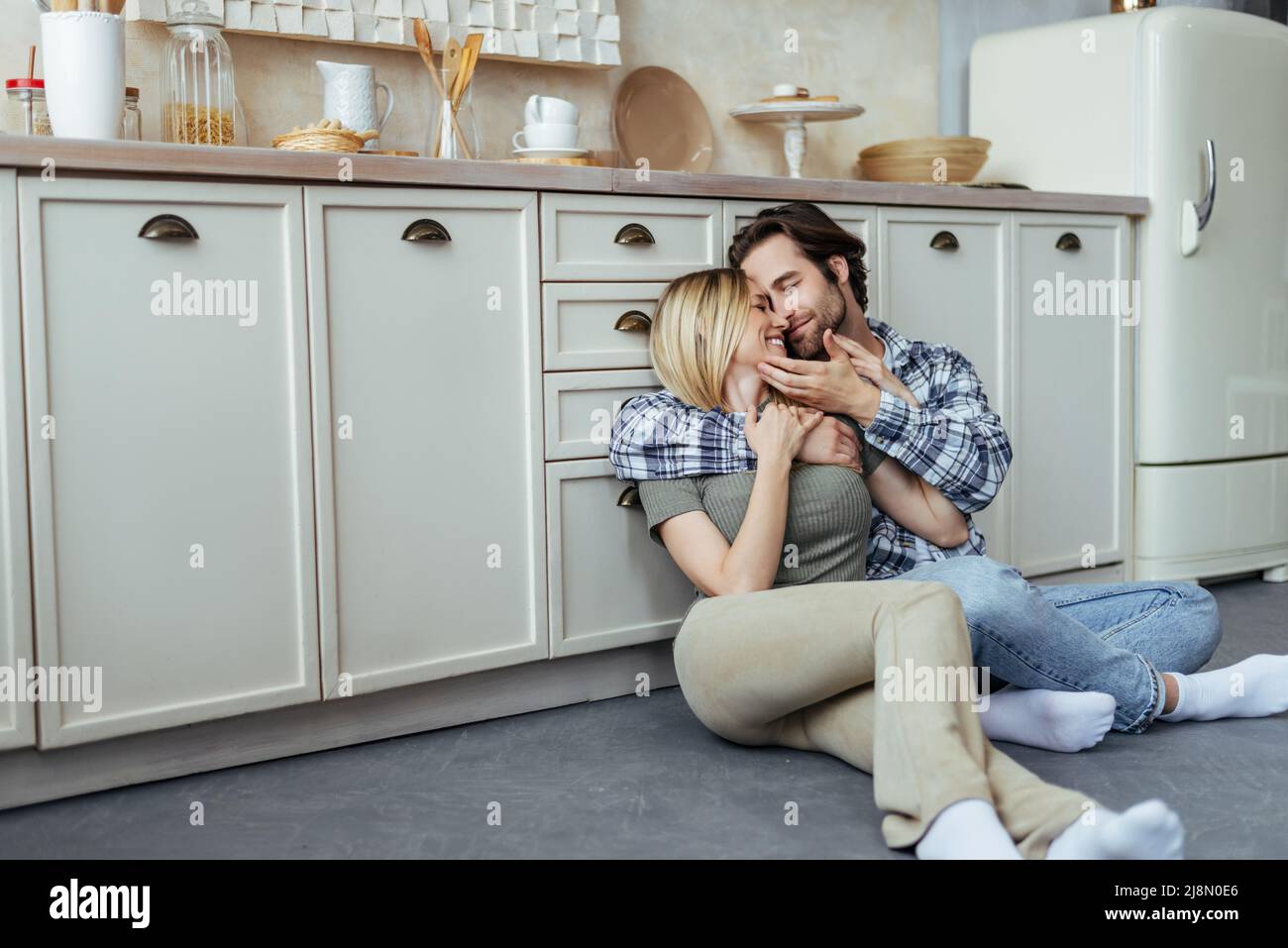 Sorridendo felice uomo europeo millenario con la moglie stoppia e bionda godere di momento tenero, abbraccio, seduto sul pavimento Foto Stock