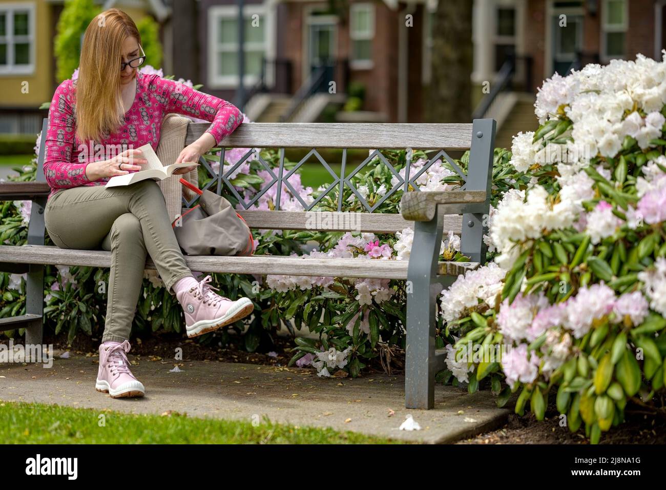 Garden City donna godendo il sole e l'aria fresca piena di profumo di fiori di primavera, mentre si siede su una panca e leggere un libro all'esterno dove la st Foto Stock