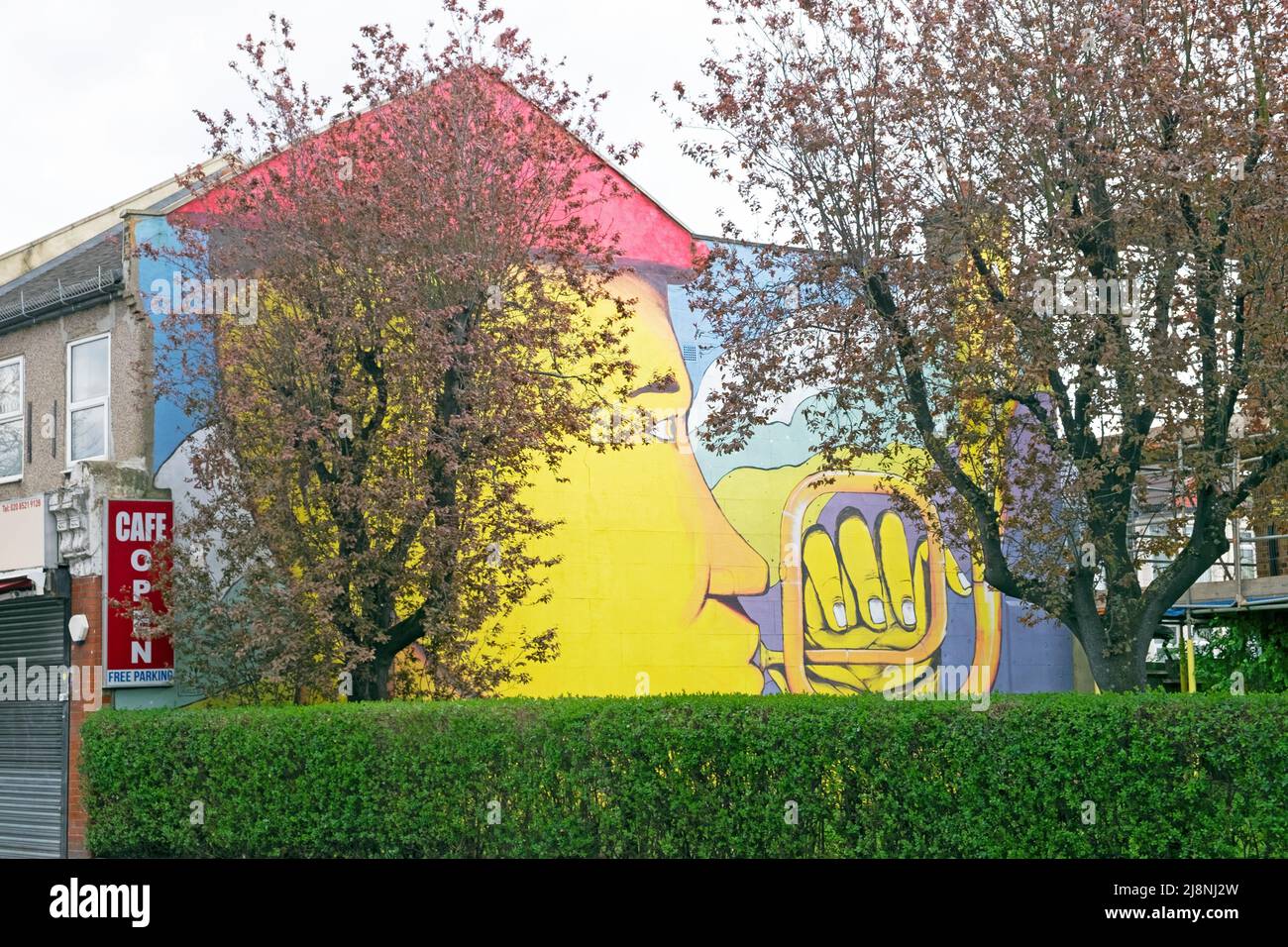 Dipinto murale a parete gialla uomo che suona strumento musicale su bordo di una fila di alloggi terrazzati vicino a Downhills Park Tottenham London UK KATHY DEWITT Foto Stock