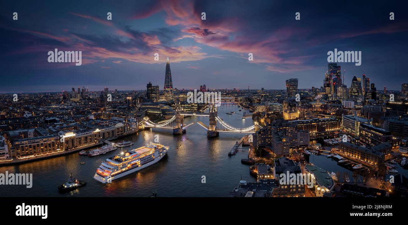 Vista aerea dello skyline di Londra con una nave da crociera con movimento sfocato che passa sotto il Ponte della Torre sollevato Foto Stock