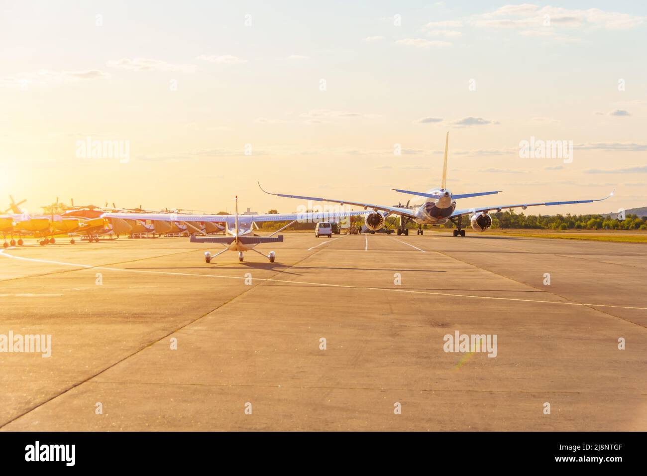 Velivolo leggero e un grande getto a corpo largo in lontananza sono tassanti per decollo, nella luce luminosa del sole che tramonta Foto Stock