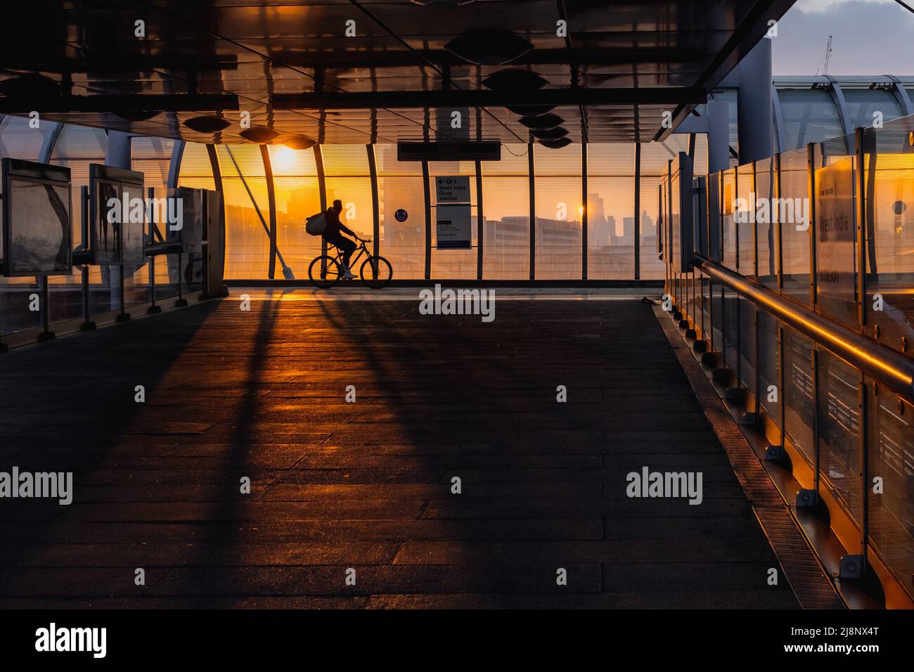 Tramonto alla stazione della ferrovia leggera Poplar Docklands nella zona est di Londra, un ciclista per la consegna di cibo lancia una silhouette. Foto Stock