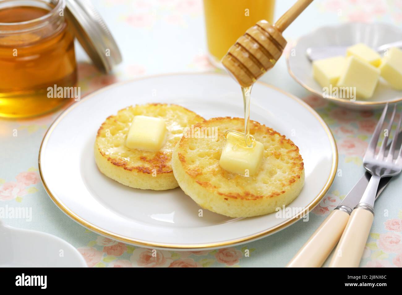 versare il miele su crumpets fatti in casa, colazione inglese Foto Stock