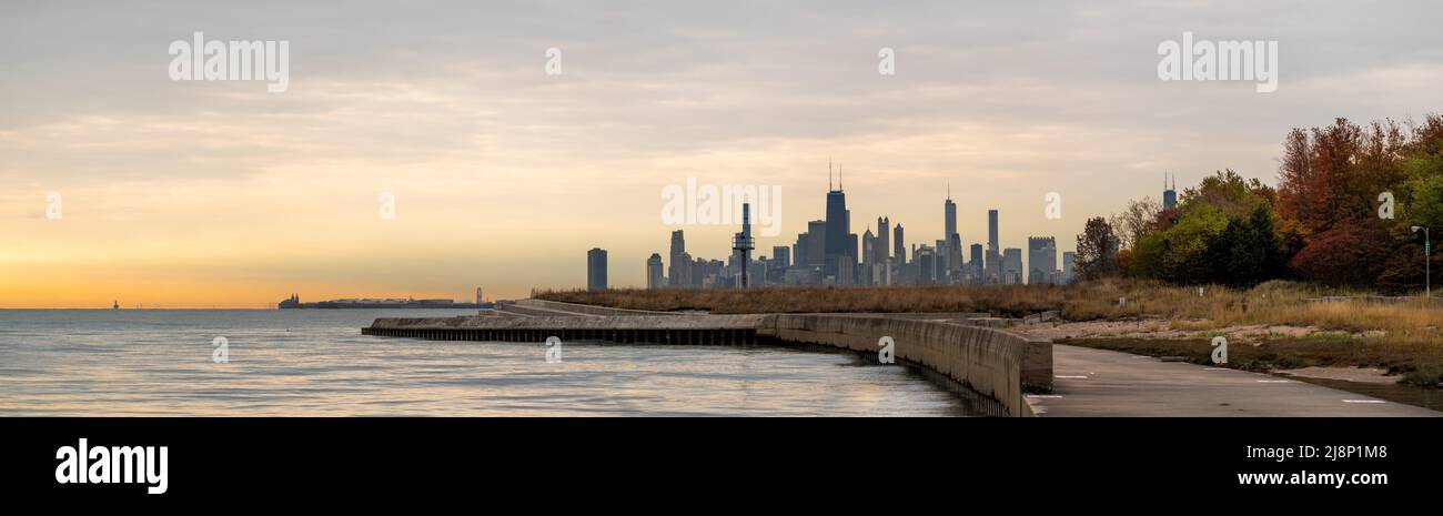 Un panorama dello skyline di Chicago all'alba con le nuvole arancioni nel cielo e l'acqua sottostante in autunno con coloratissime foglie di alberi. Foto Stock