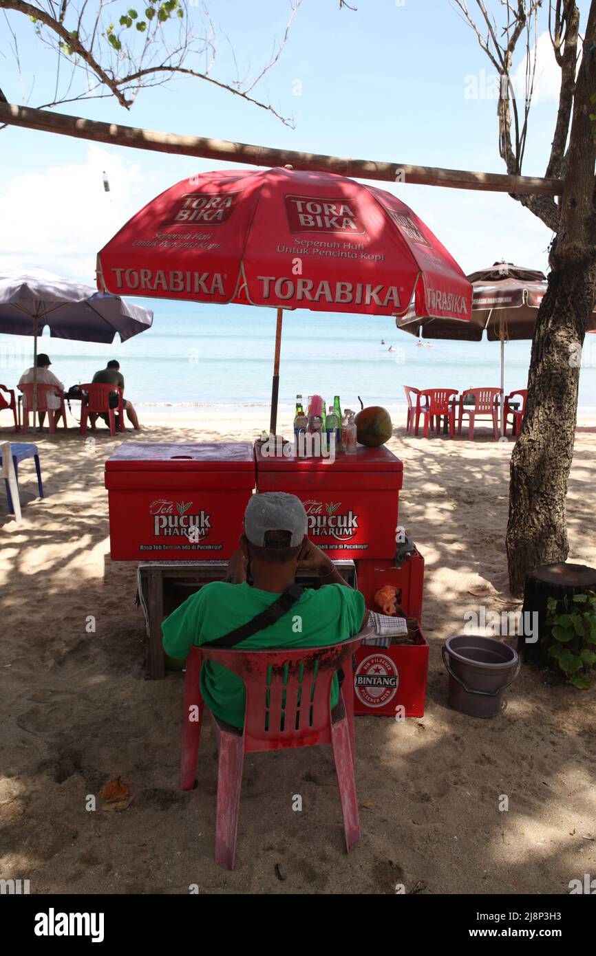 Un rivenditore di bevande a Kuta Beach a Bali, Indonesia, seduto all'ombra degli alberi durante la pandemia nel marzo 2022. Foto Stock