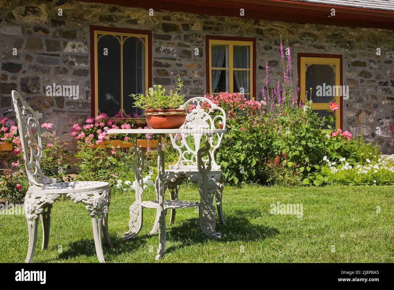 Sedie da giardino vittoriano in ghisa bianca e tavolo sul prato anteriore del vecchio regime 1794 francese casa in pietra da campo in stile casale in estate. Foto Stock