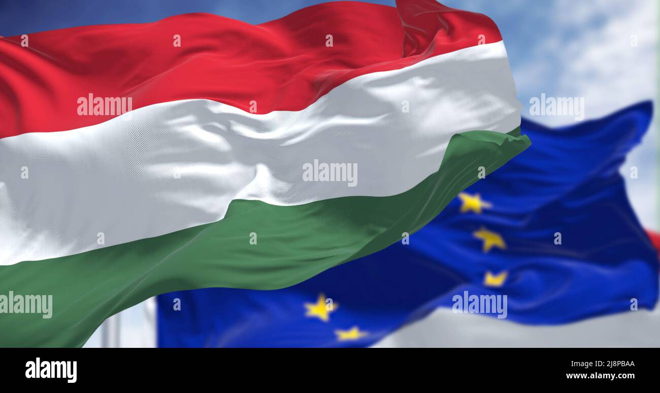 Dettaglio della bandiera nazionale dell'Ungheria che sventola nel vento con la bandiera dell'Unione europea sfocata sullo sfondo in una giornata chiara. Democrazia e politica. E Foto Stock