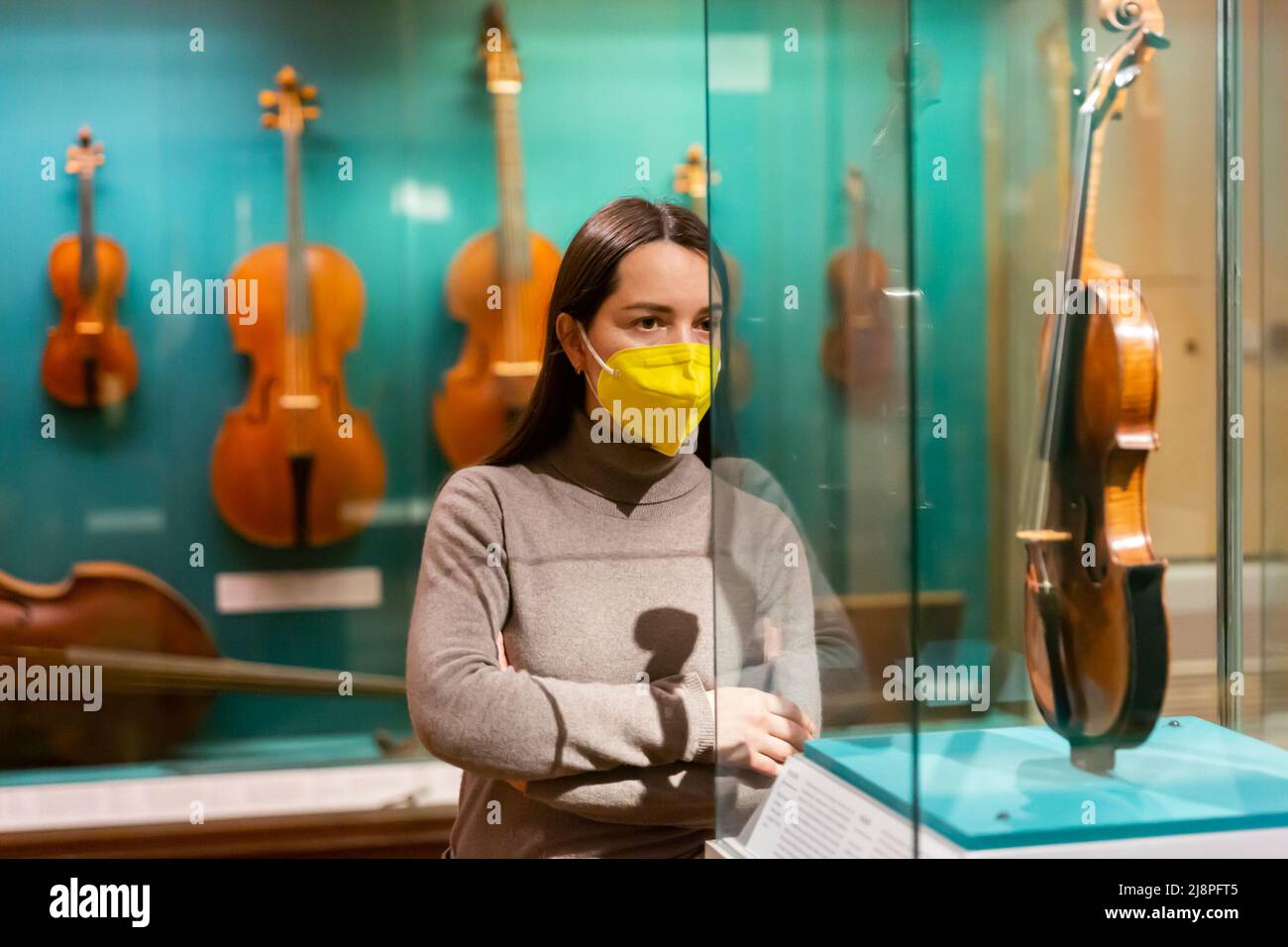 Donna in maschera che guarda collezioni di antichi strumenti musicali in museo Foto Stock
