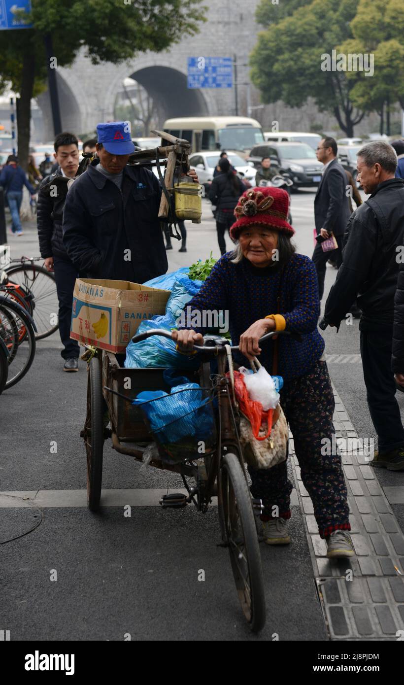 Una donna cinese anziana che spinge la sua bicicletta carica nel centro della città di Nanjing, Cina. Foto Stock