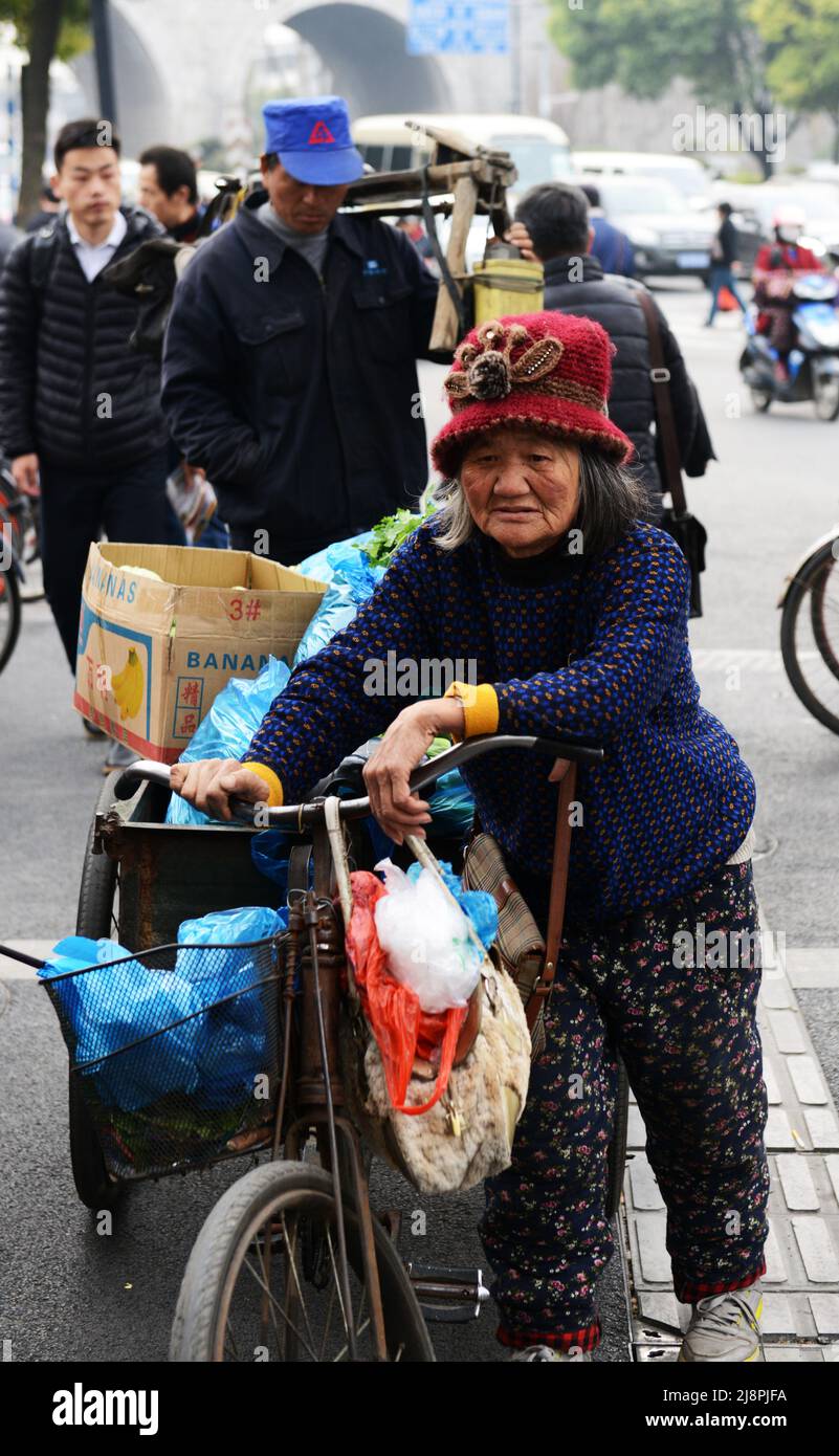 Una donna cinese anziana che spinge la sua bicicletta carica nel centro della città di Nanjing, Cina. Foto Stock