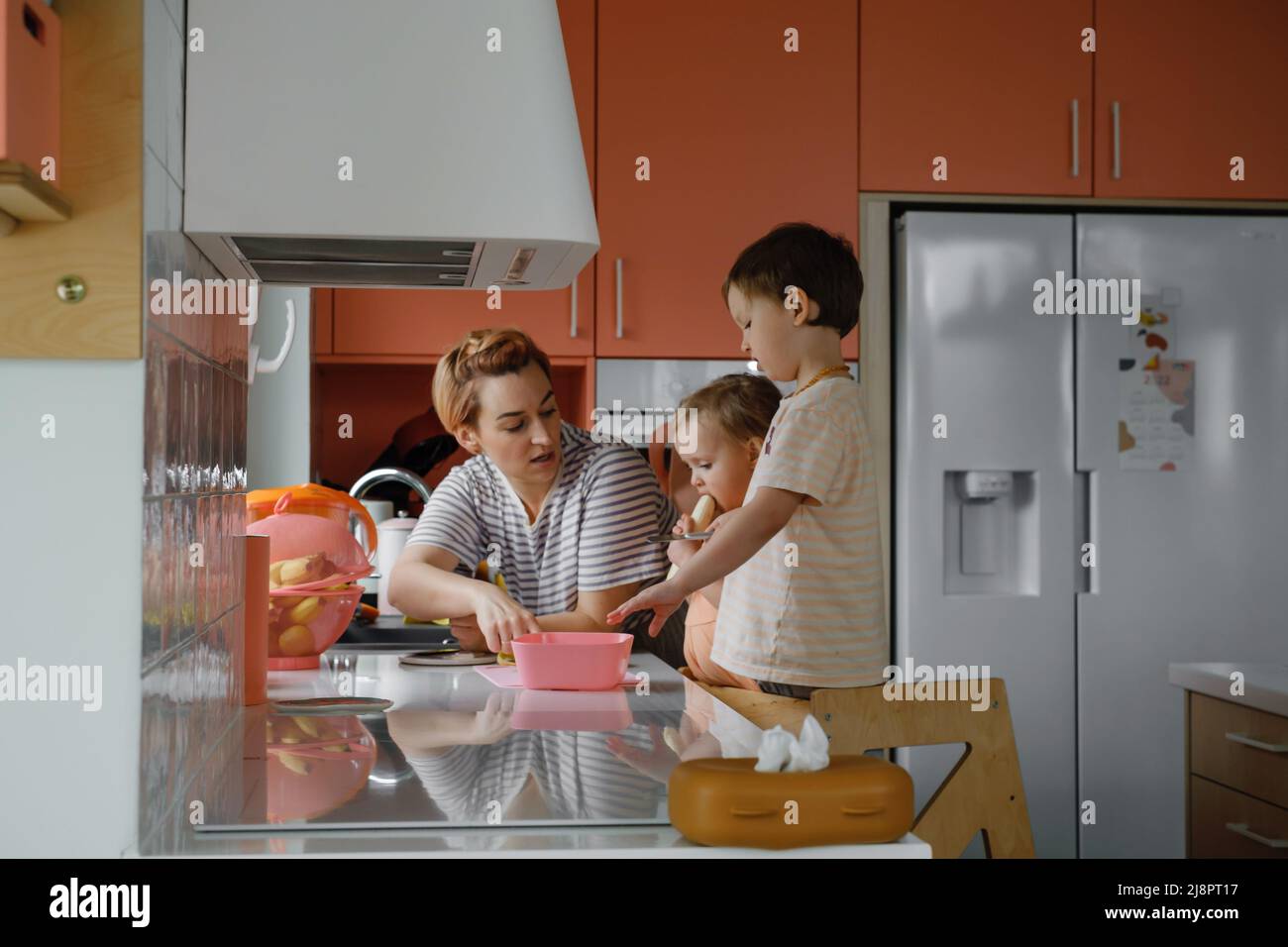 Famiglia felice con i bambini che cucinano sulla cucina moderna. Bambini che tagliano Macedonia di frutta, preparando cibo con madre e padre. Mangiare sano a casa Foto Stock