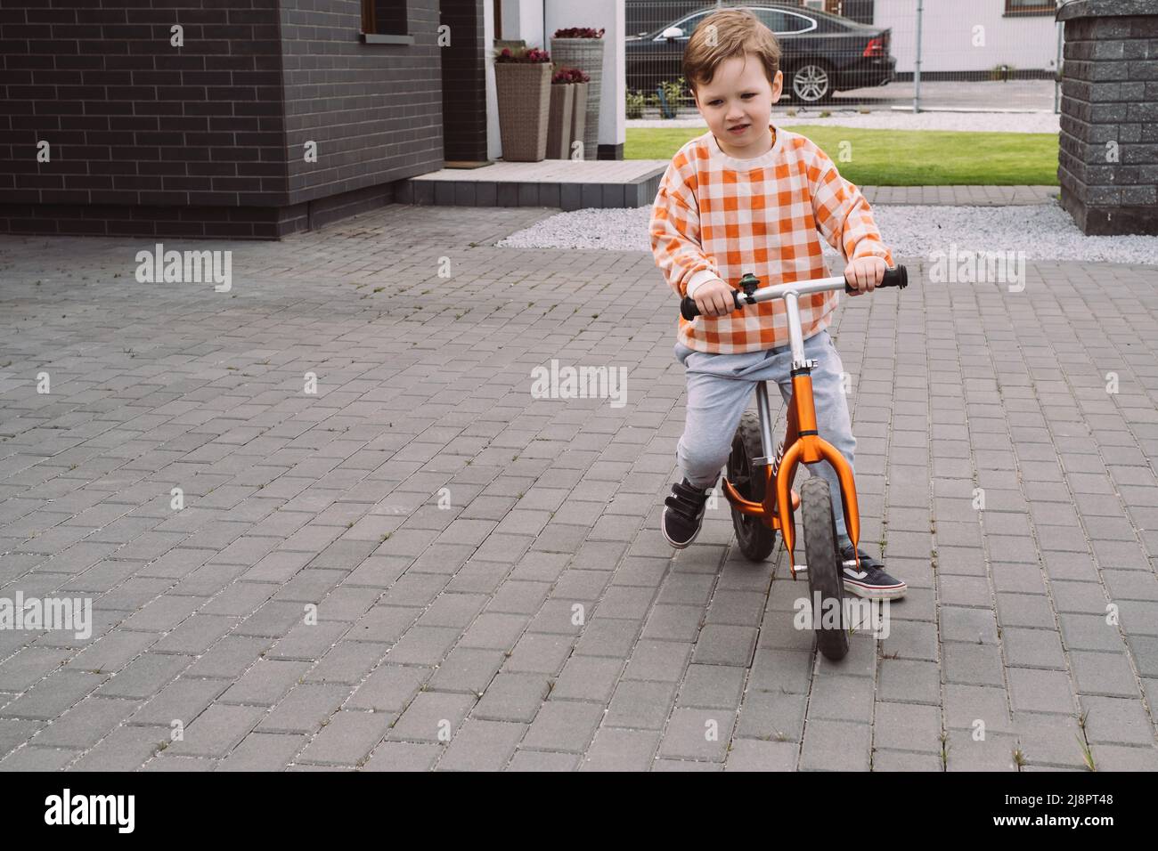 Bambino che gioca a corse in bicicletta nel cortile di casa. Ragazzo a cavallo veloce intorno casa privata. Concorsi di giochi per famiglie. Attività sportive per bambini all'aperto nelle vicinanze Foto Stock