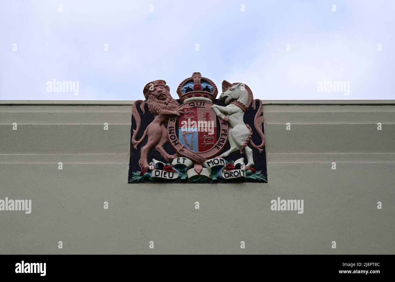 Stemma reale del Regno Unito, in cima alla parete esterna bianca di un edificio, con cielo nuvoloso sullo sfondo Foto Stock