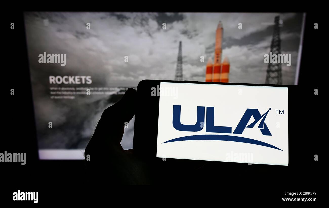 Persona che tiene uno smartphone con il logo della United Launch Alliance (ULA) della società spaziale statunitense sullo schermo di fronte al sito Web. Mettere a fuoco sul display del telefono. Foto Stock