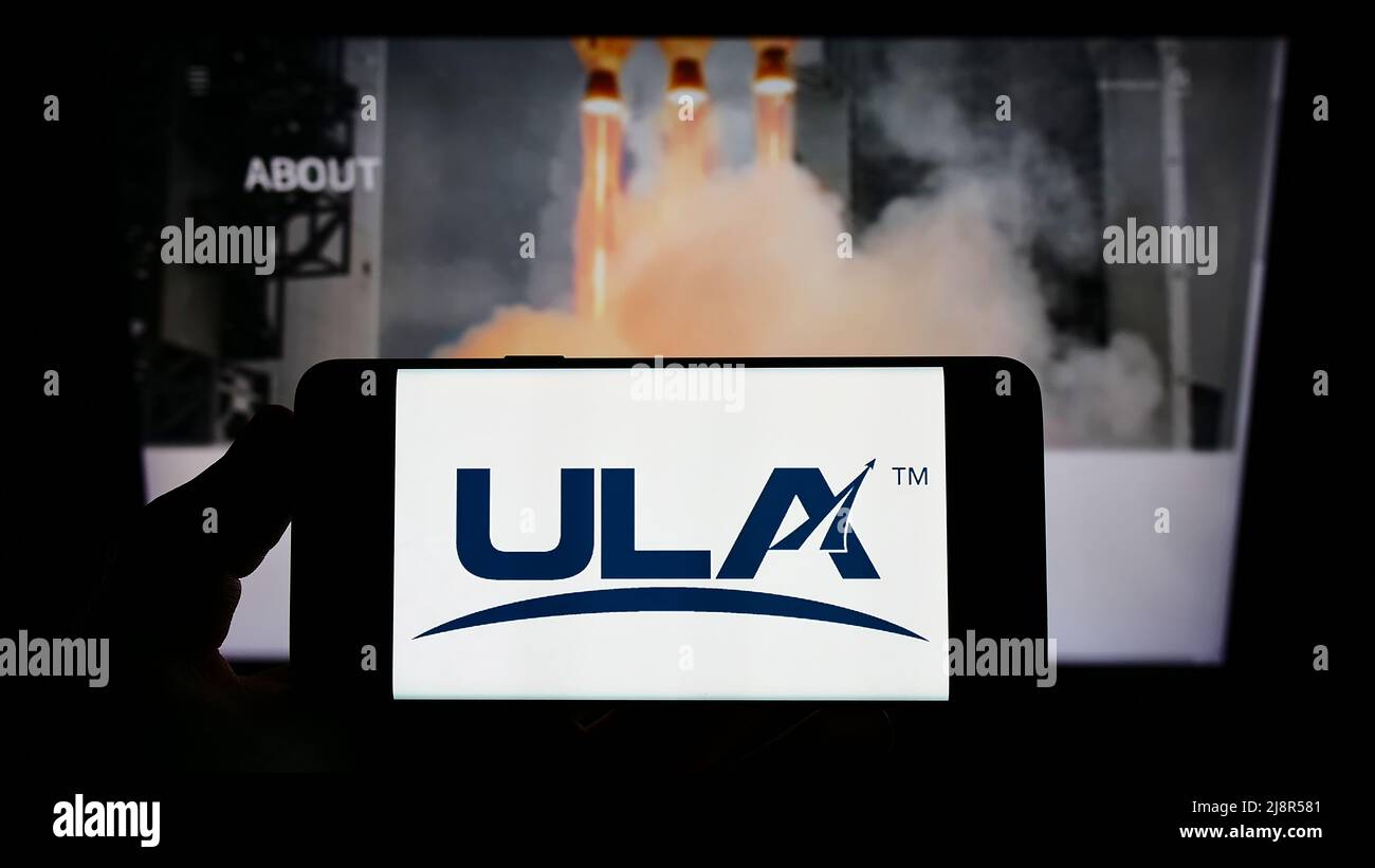 Persona che detiene il telefono cellulare con il logo della United Launch Alliance (ULA) della società spaziale statunitense sullo schermo di fronte alla pagina Web. Mettere a fuoco sul display del telefono. Foto Stock