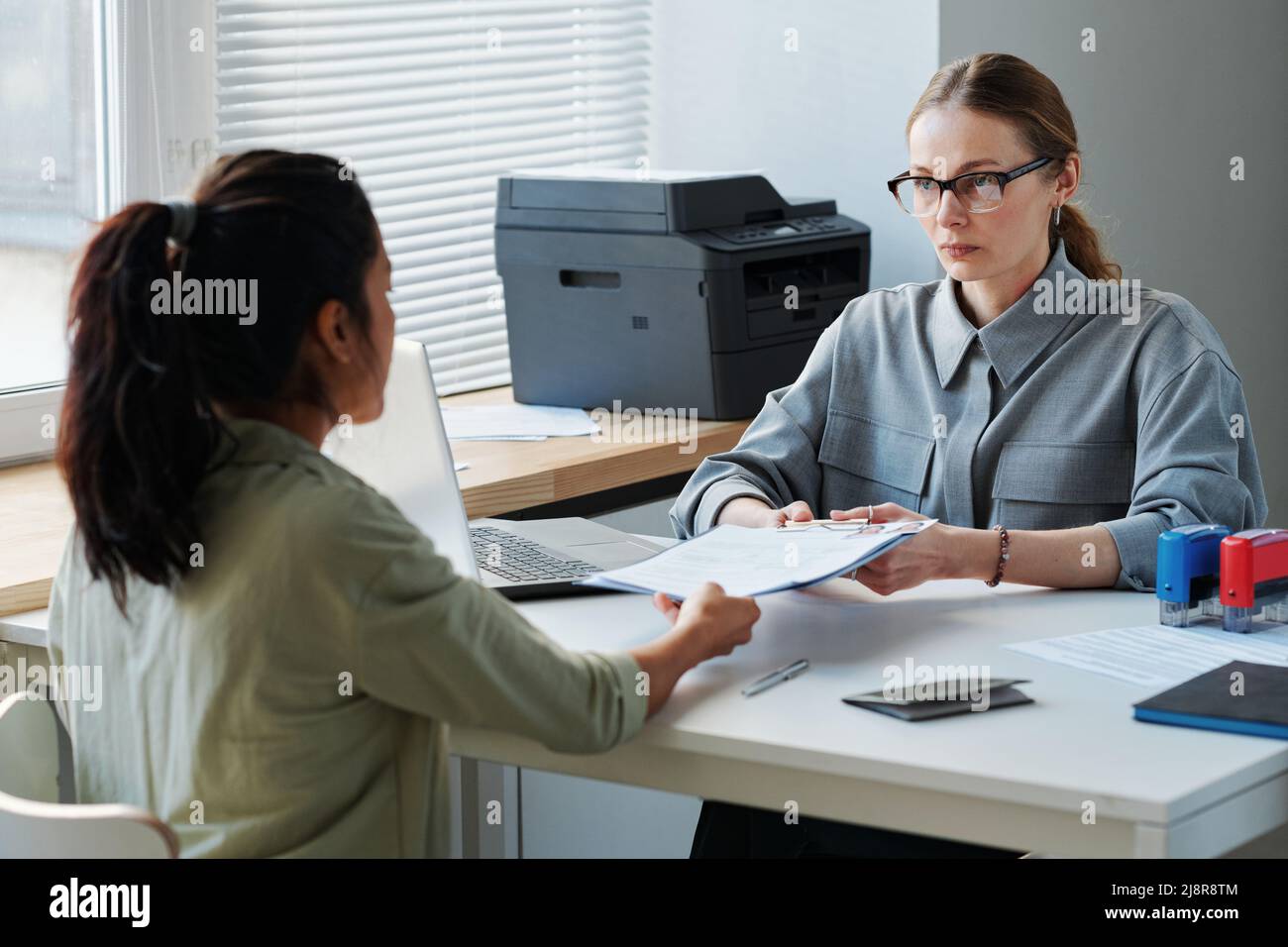 Donna irriconoscibile che fa domanda per il visto di lavoro o di visita che dà insieme dei documenti all'ufficiale consolare professionale Foto Stock