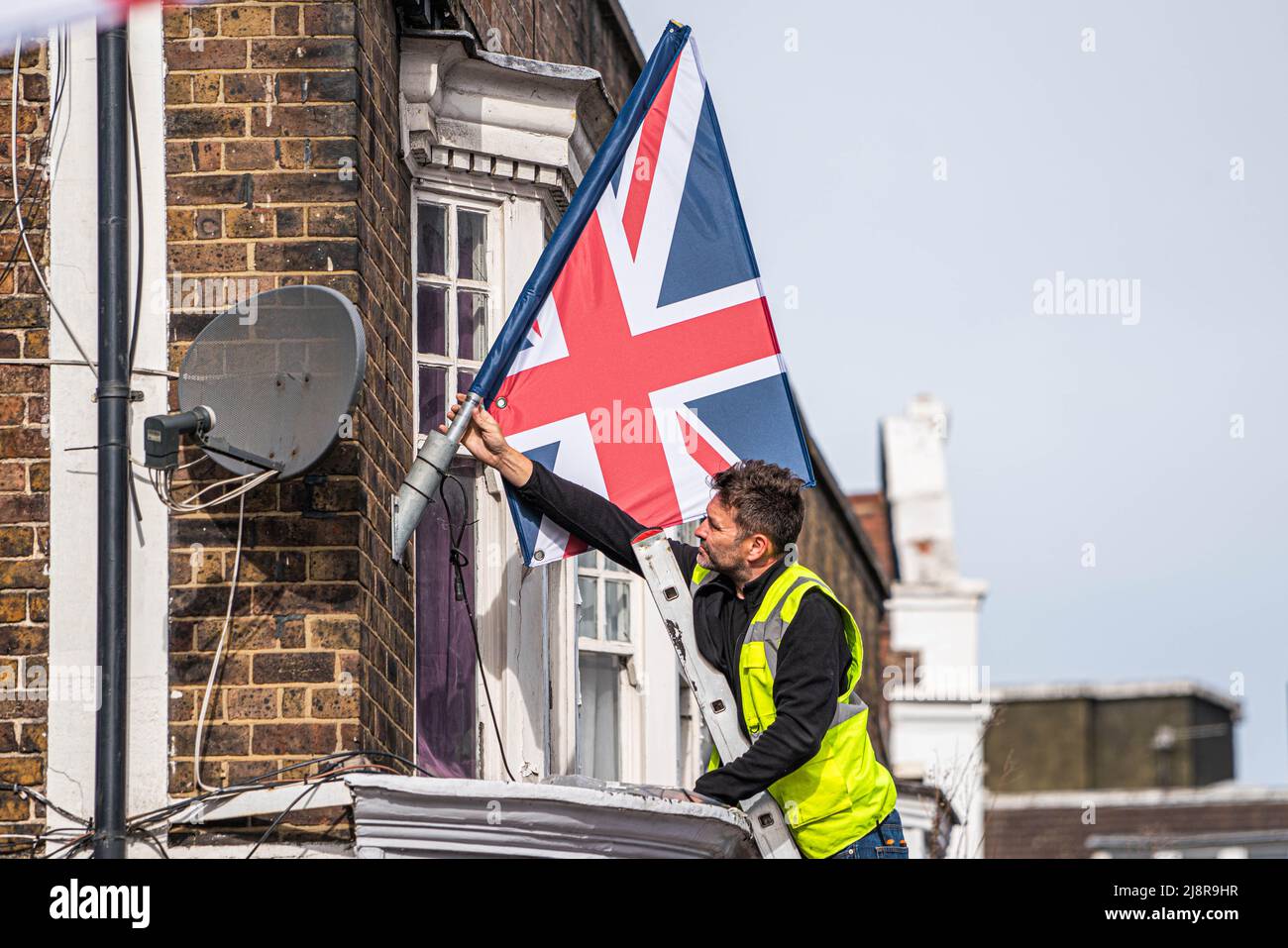 Londra UK, 18 maggio 2022. Un'operatrice del consiglio pone un Union Jack su un flagpole nel villaggio di Wimbledon per celebrare il Giubileo del platino mentre la regina Elisabetta segna 70 anni sul trono come il più lungo serving dei monarchi britannici Credit. amer Ghazzal/Alamy Live News Foto Stock