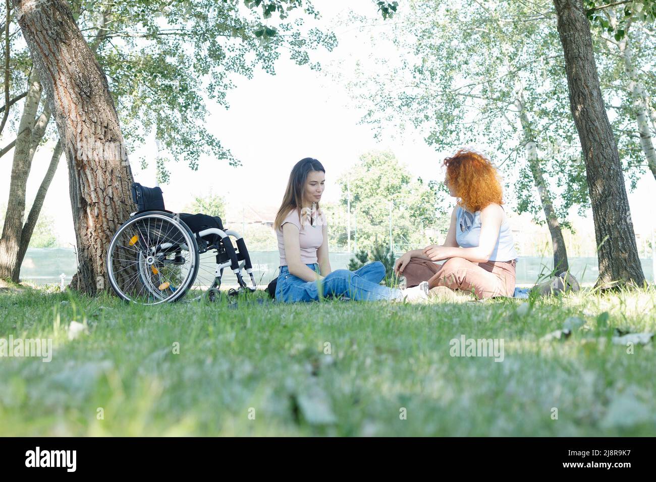 Una persona con disabilità e la sua amica femmina che ha una piacevole conversazione in un'ombra di alberi di pioppo Foto Stock