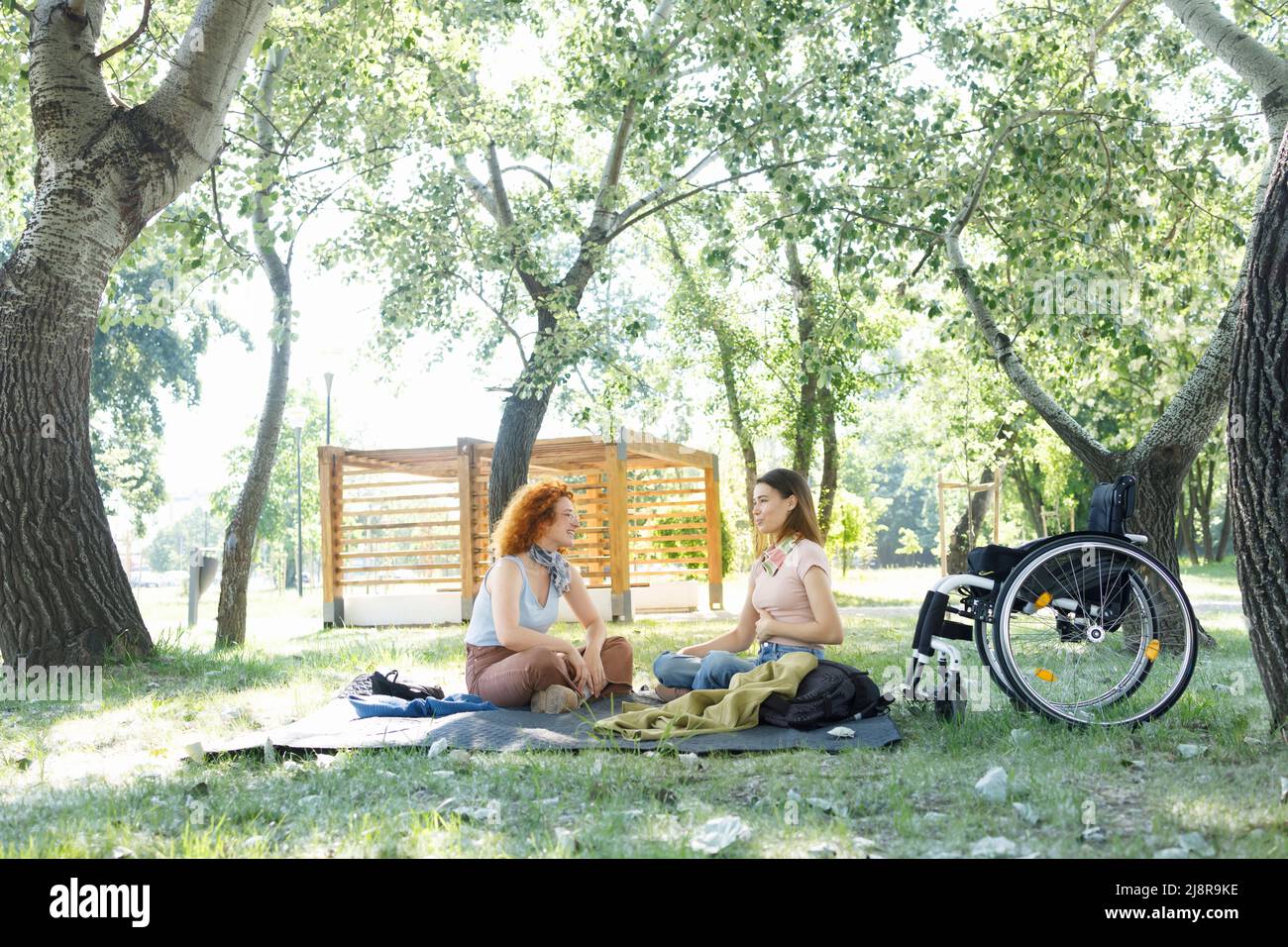 Due amiche che hanno una conversazione in un parco pubblico durante una piacevole giornata estiva Foto Stock