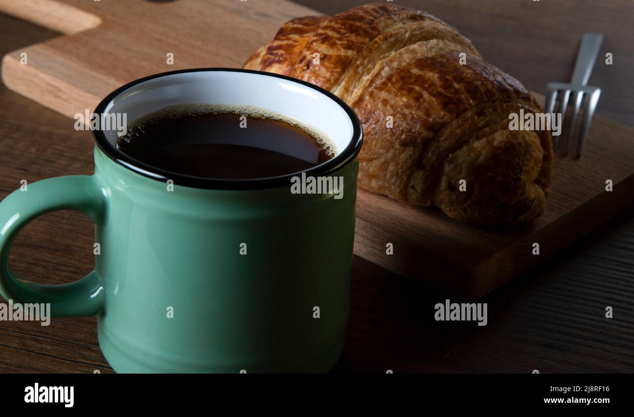 Tazza di caffè e croissant su sfondo di legno Foto Stock