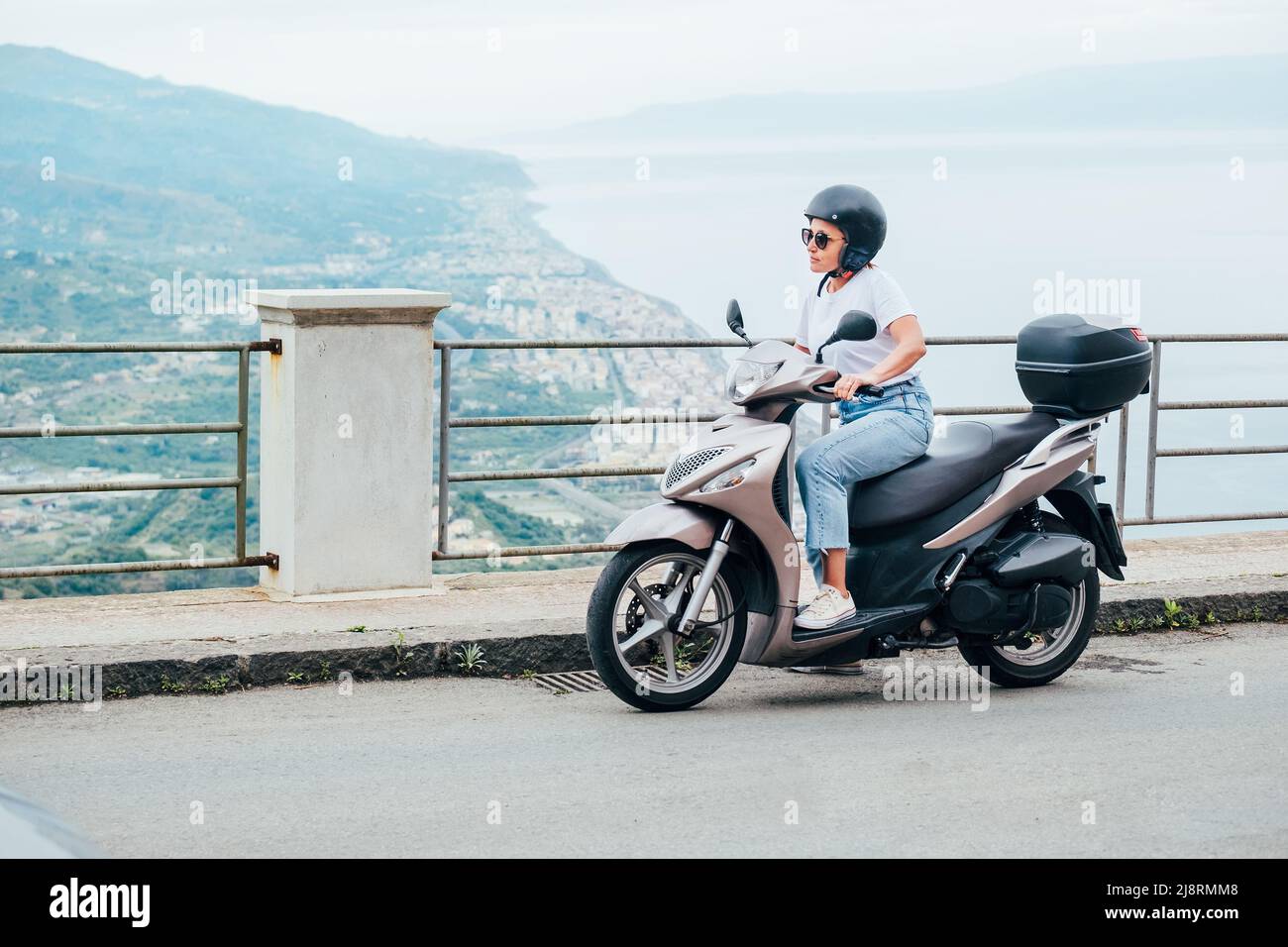 Donna di mezza età in casco e occhiali da sole su scooter a motore sulle  strade