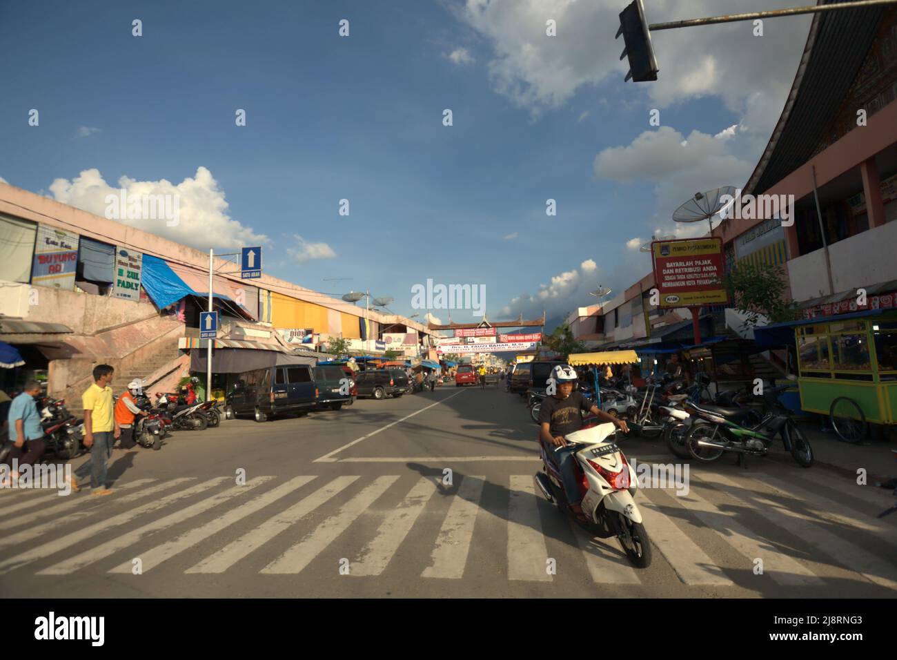 Un motorista che guida sulla strada, attraversando una croce zebra in un'area commerciale a Payakumbuh, Sumatra occidentale, Indonesia. Foto Stock