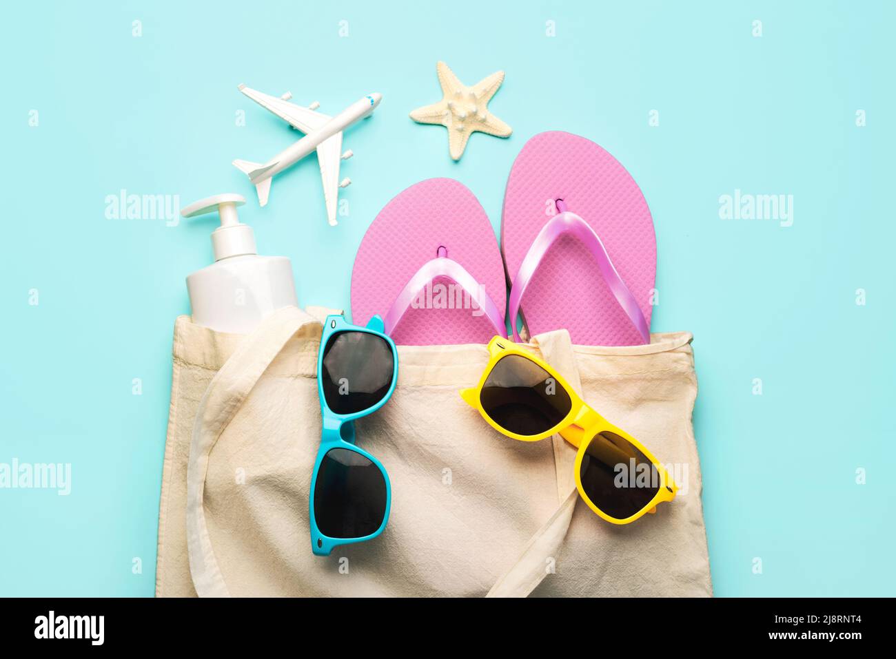 Estate vacanza Concept.Top vista della borsa da spiaggia con infradito, occhiali da sole, crema solare, aeroplano e stelle marine su sfondo blu Foto Stock